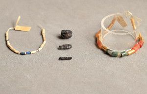 Three ancient Egyptian beads made of iron from a meteorite sit between examples of other beads that they were strung with, including lapis lazuli (blue), carnelian (brownish red), agate (green and white) and gold.