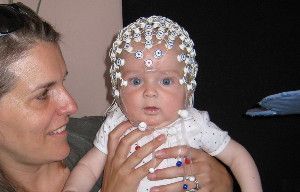 Infants, including this 5-month-old boy fitted with an electrode-covered cap and held by his mother, display electrical brain responses possibly representing visual awareness, a new study finds.