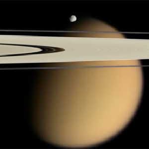 Saturn's moon Titan (orange, in background) seems to have lakes of methane near the equator, as well as at the poles.